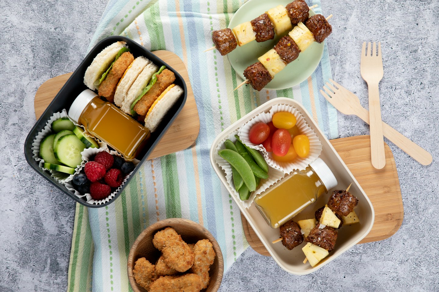 Otwarte pudełka na lunch ze zdrowymi przekąskami na pasiastym obrusie.